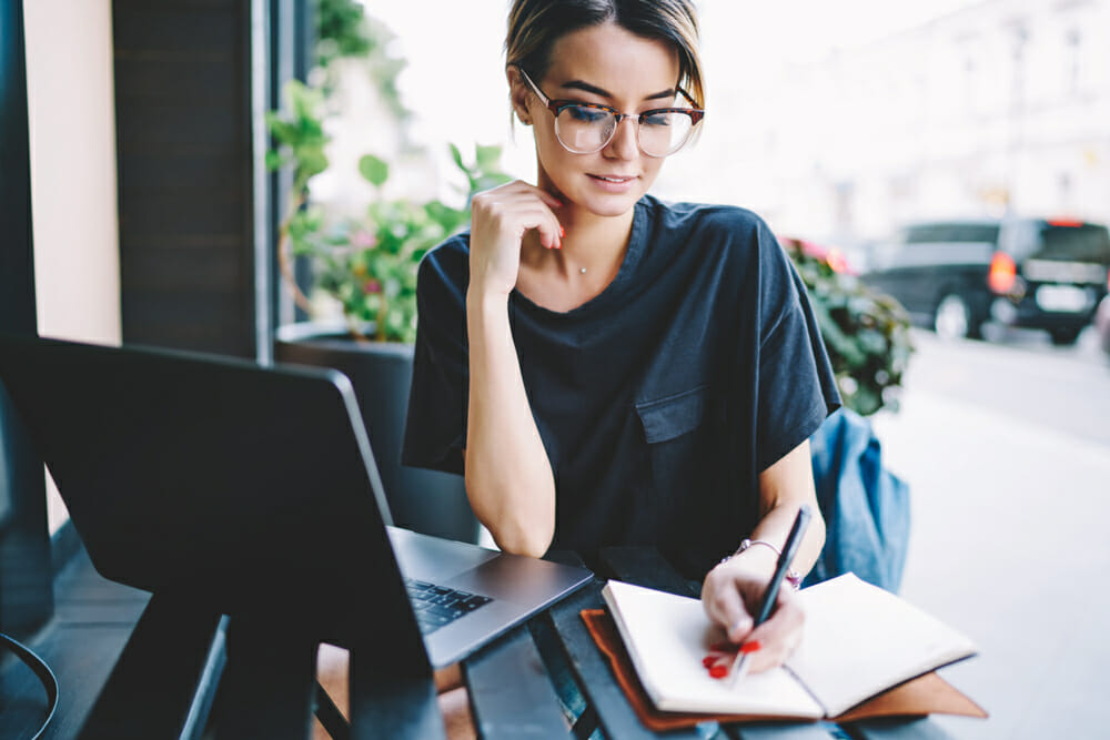 Woman sitting at an outdoor table writing in a notebook