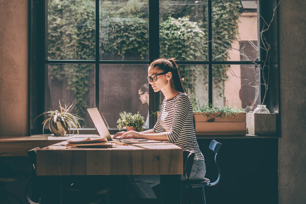 Woman sitting at a table in front of windows with her laptop