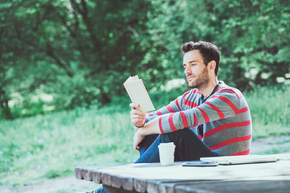 Man sitting outside reading a book on the grass