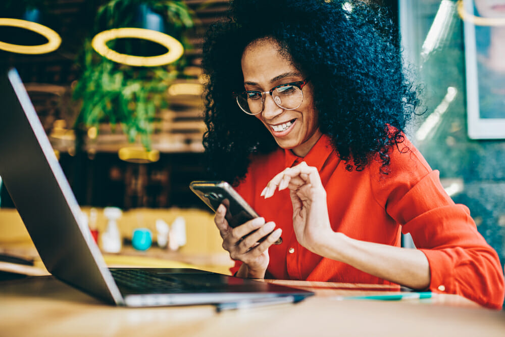 Woman sitting at a desk on her smartphone in front of a computer