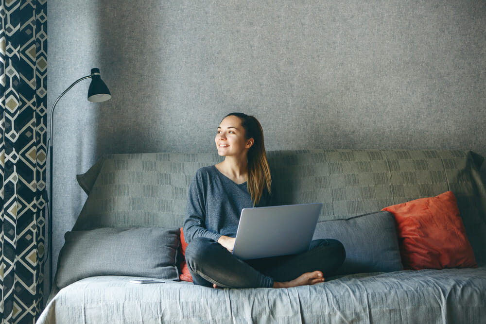 Woman sitting on a couch with her laptop looking out her window