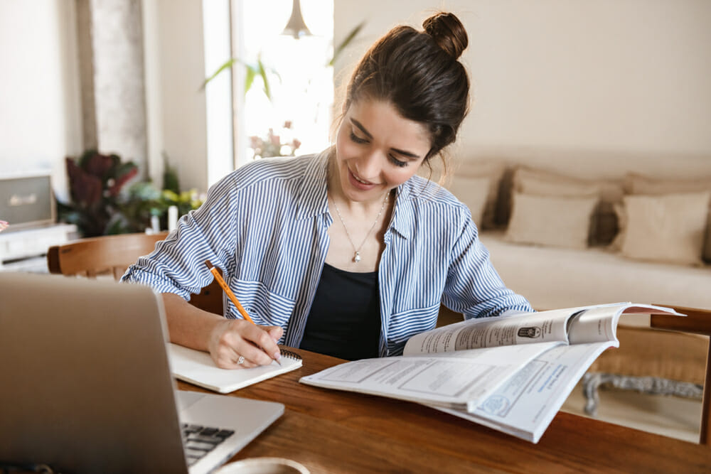 Woman sitting at a desk with a book, pencil and laptop