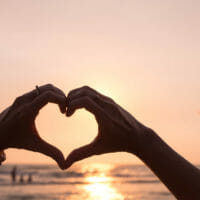 person making a heart with their hands over the ocean
