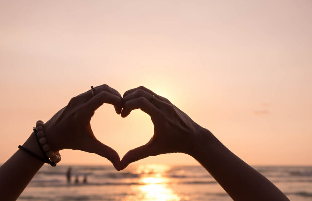 person making a heart with their hands over the ocean