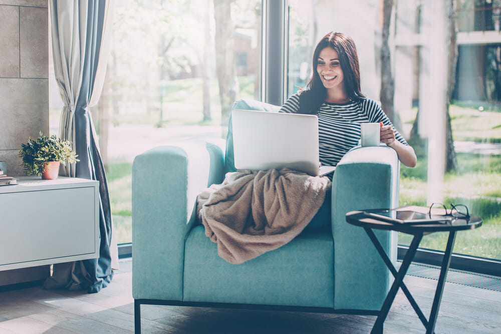 Woman sitting on cozy chair with a blanket and laptop