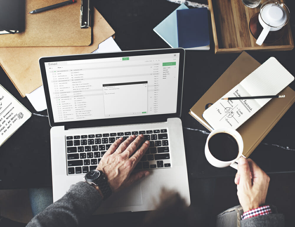 person typing an email with a cup of coffee