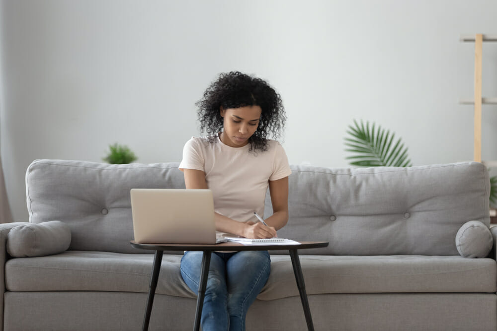 Woman sitting on her couch with a piece of paper and laptop