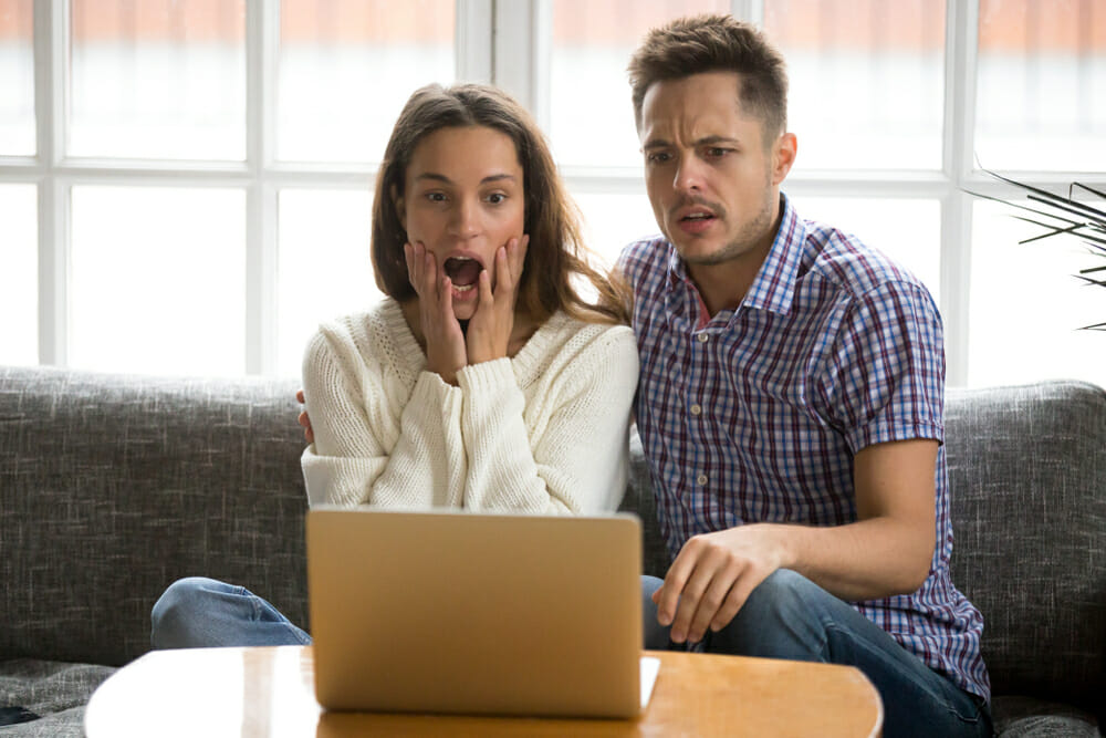 Man and woman sitting in front of their laptop looking shocked