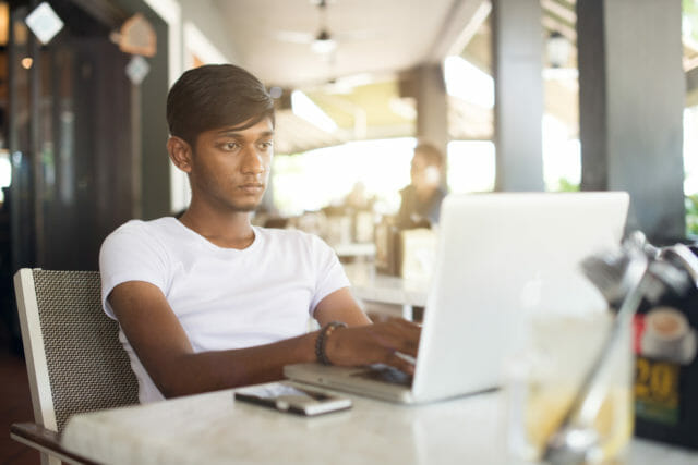 Man sitting in a cade looking at his laptop