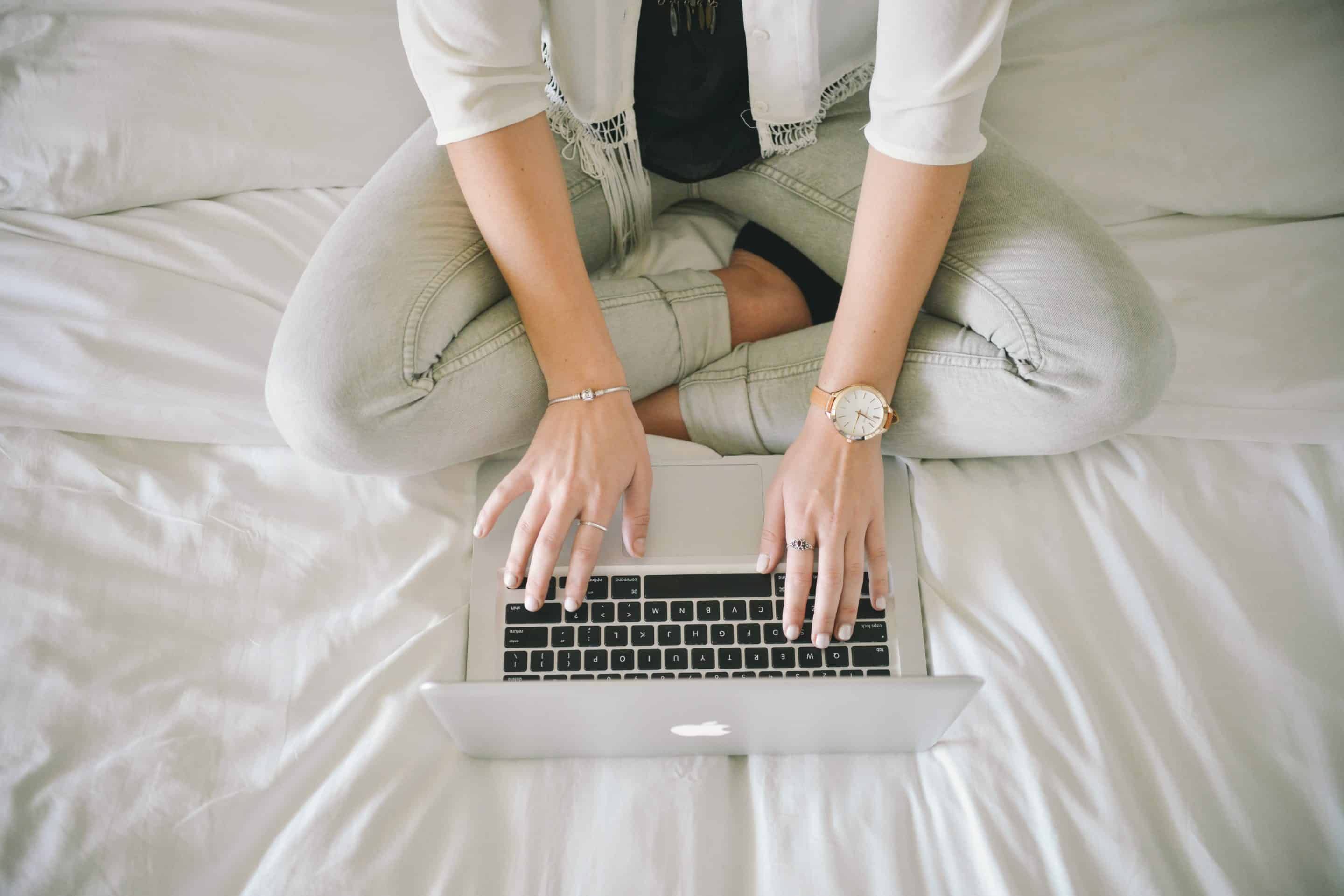 woman sitting cross-legged typing on a bed