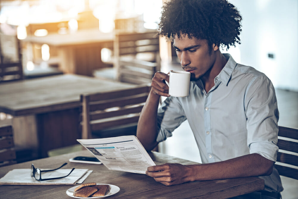Man reading a newspaper and drinking a cup of coffee