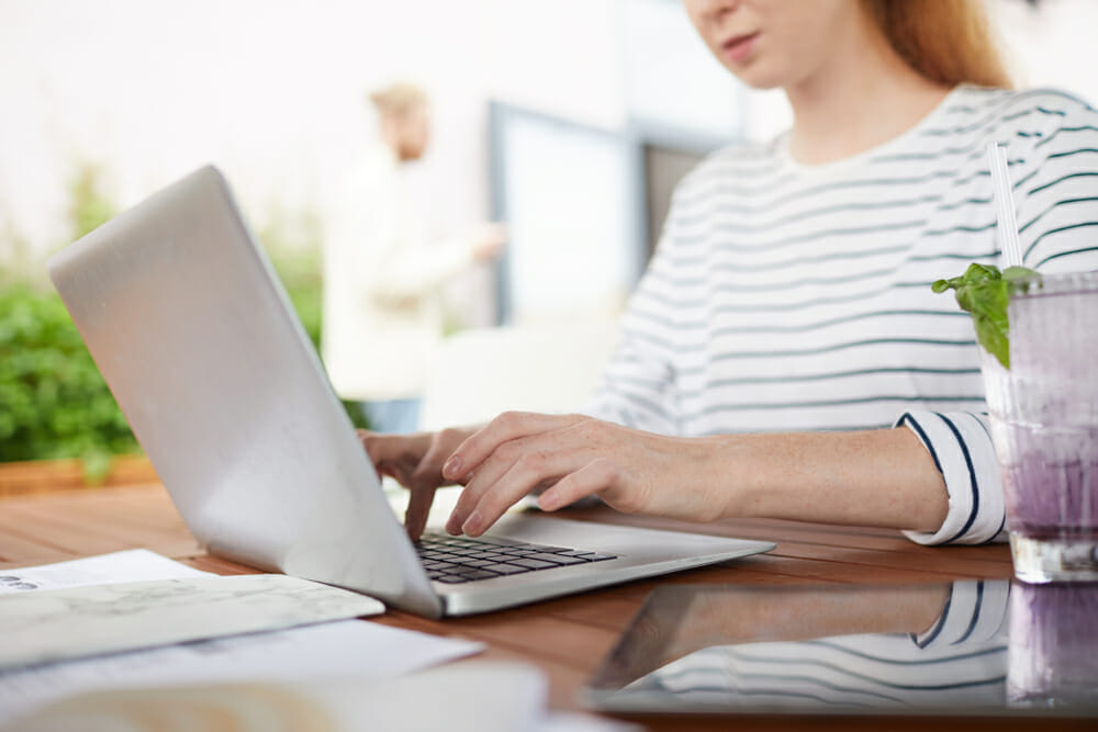 woman typing on a laptop with a drink next to her