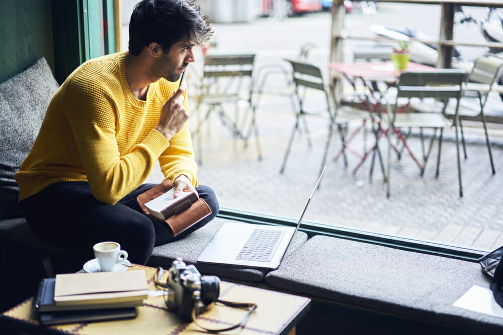 Man sitting at a coffee shop with laptop and notebook