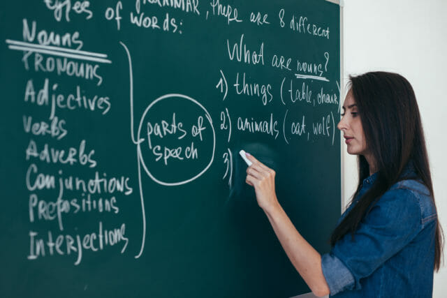 Woman standing in front of a chalkboard teaching grammar