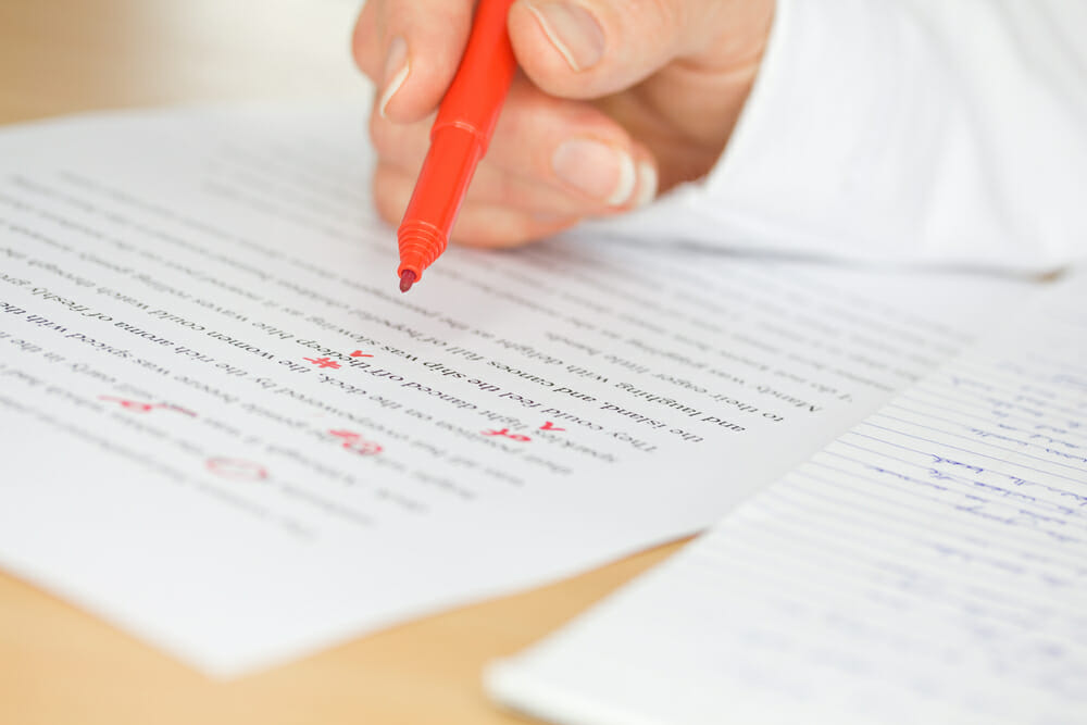 Person holding a red pen proofreading a paper