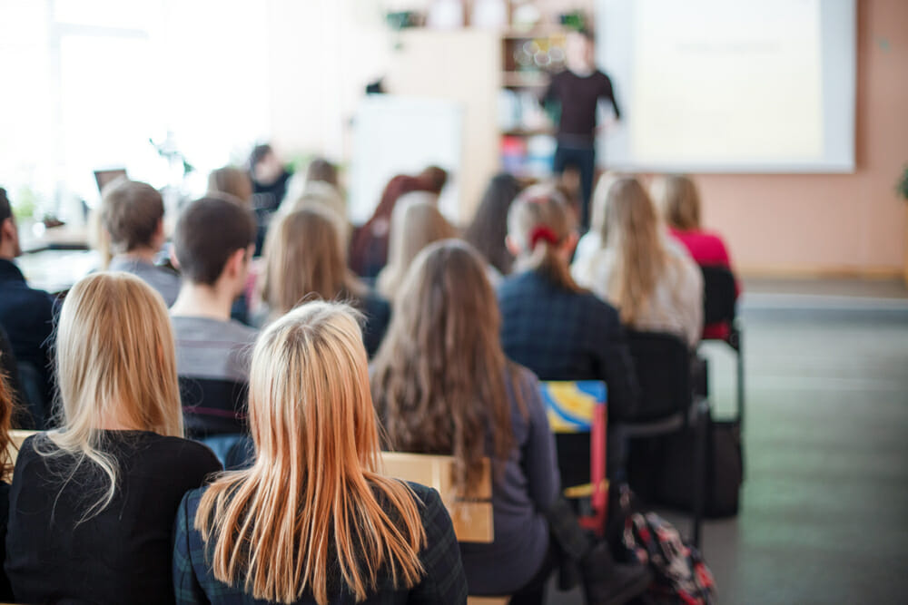 Students sitting in a classroom listening to a teacher