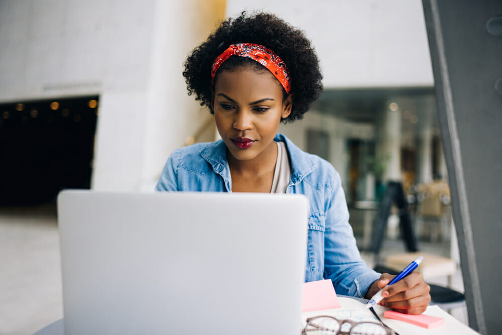 Woman sitting in front of her laptop writing on a notepad