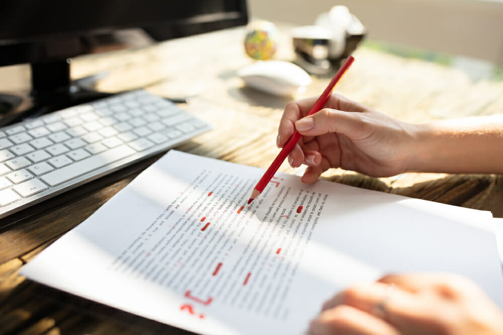 Person with a red pencil underlining lines on a piece of paper