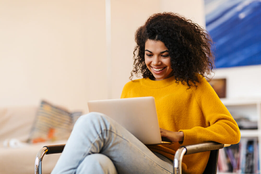 Woman sitting in a char smiling down at her laptop