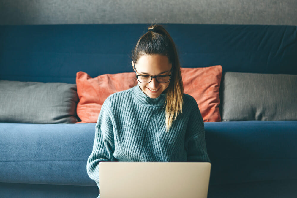 Woman sitting on the floor in front of a couch on her laptop