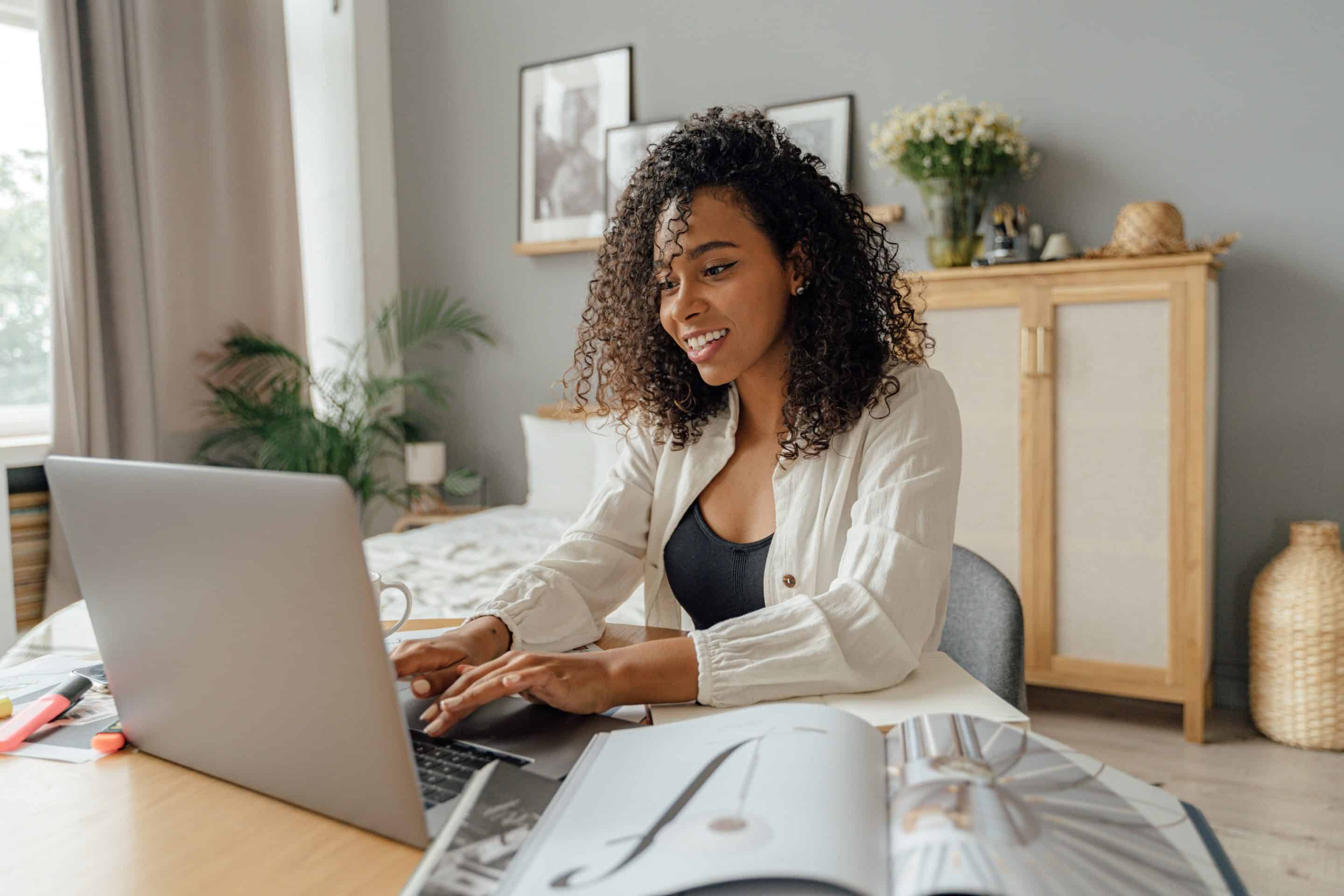 Woman sitting at a desk with her laptop and a book open in front of her.