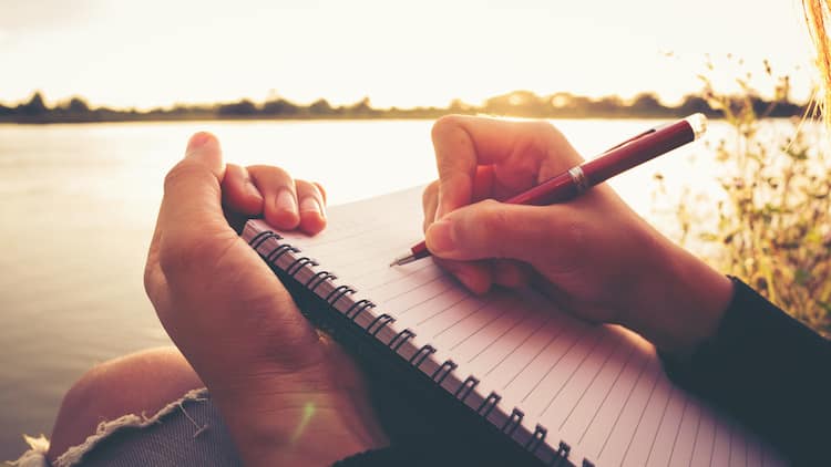 journaling prompts for writers - woman writing in journal by a lake