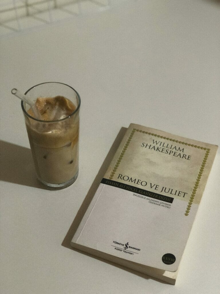 Overhead photograph of an iced coffee beverage with a straw sitting next to a paperback copy of William Shakespeare's Romeo and Juliet. One of the words invented by Shakespeare appears in this play—alligator, believe it or not.